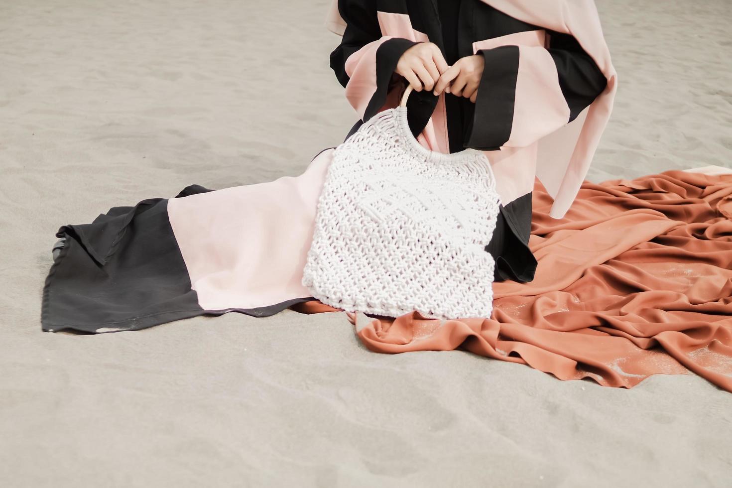 Beautiful islamic female model wearing hijab fashion, a modern wedding dress for muslim woman sitting in the sand and beach. Portrait an asian girl model using hijab having fun at the beach with trees photo