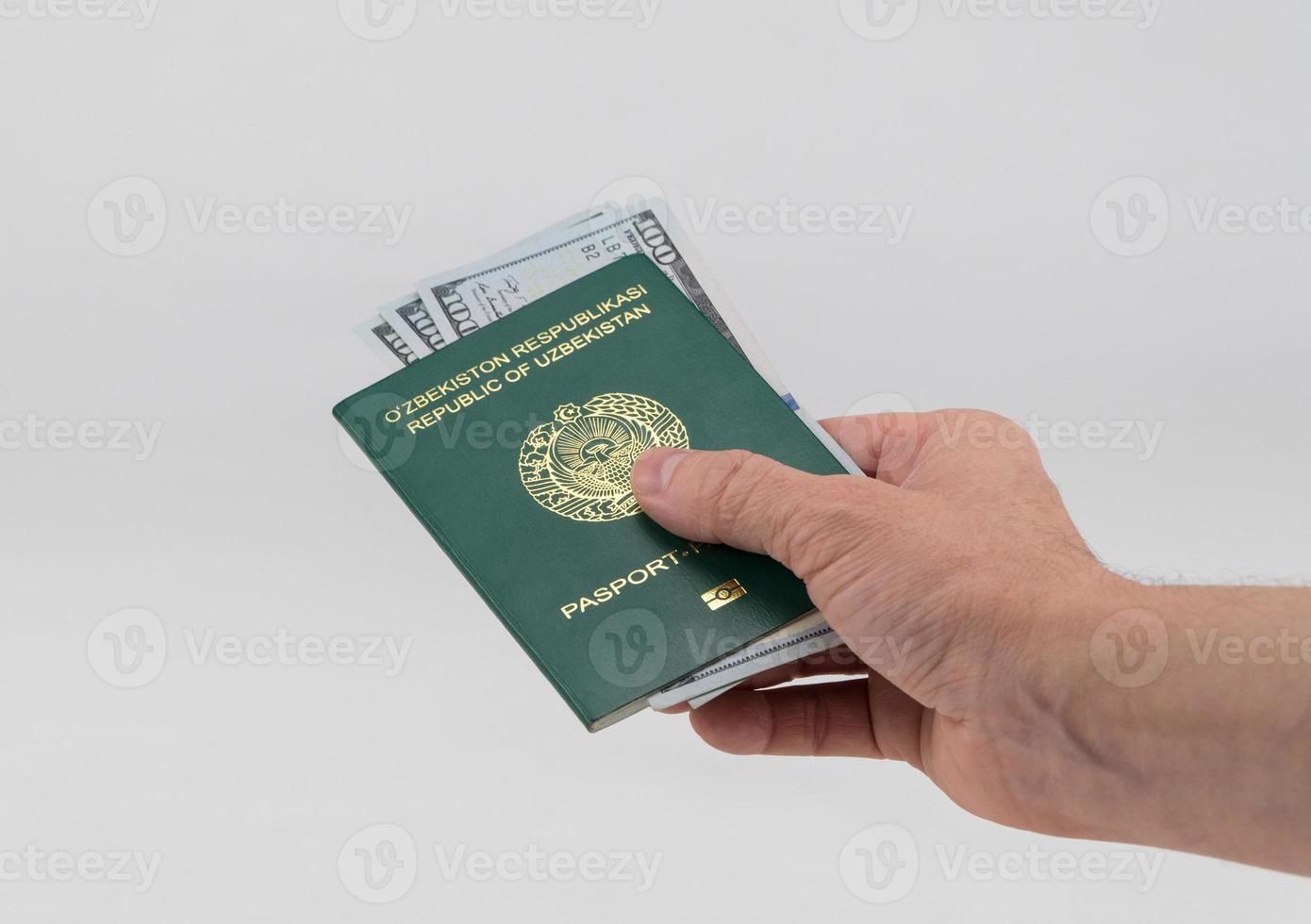 la mano sostiene el pasaporte de uzbekistán con dólares estadounidenses. concepto - soborno y corrupción foto