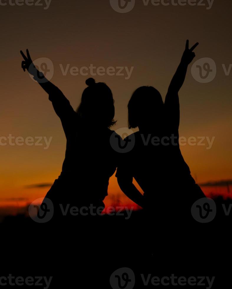 Silhouette of girls make heart with their hand. Happy friendship concept. photo