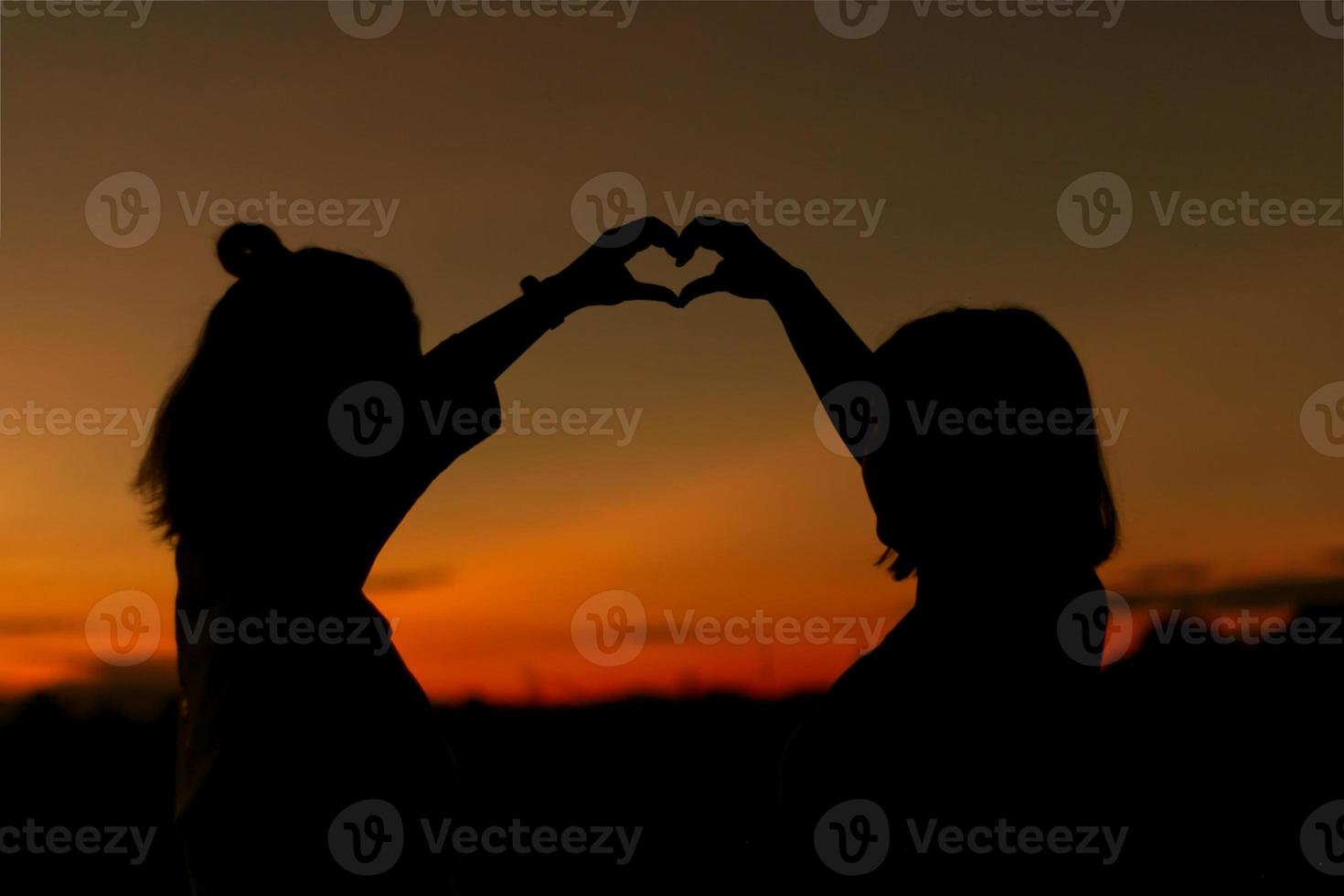 Silhouette of girls make heart with their hand. Happy friendship concept. photo