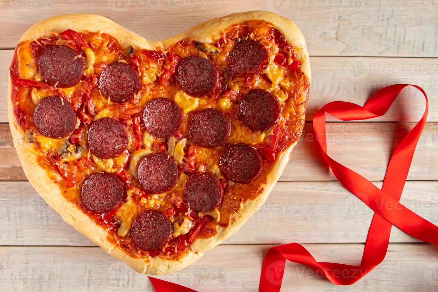 Heart shaped pepperoni pizza on wooden background. Valentines day gift. photo