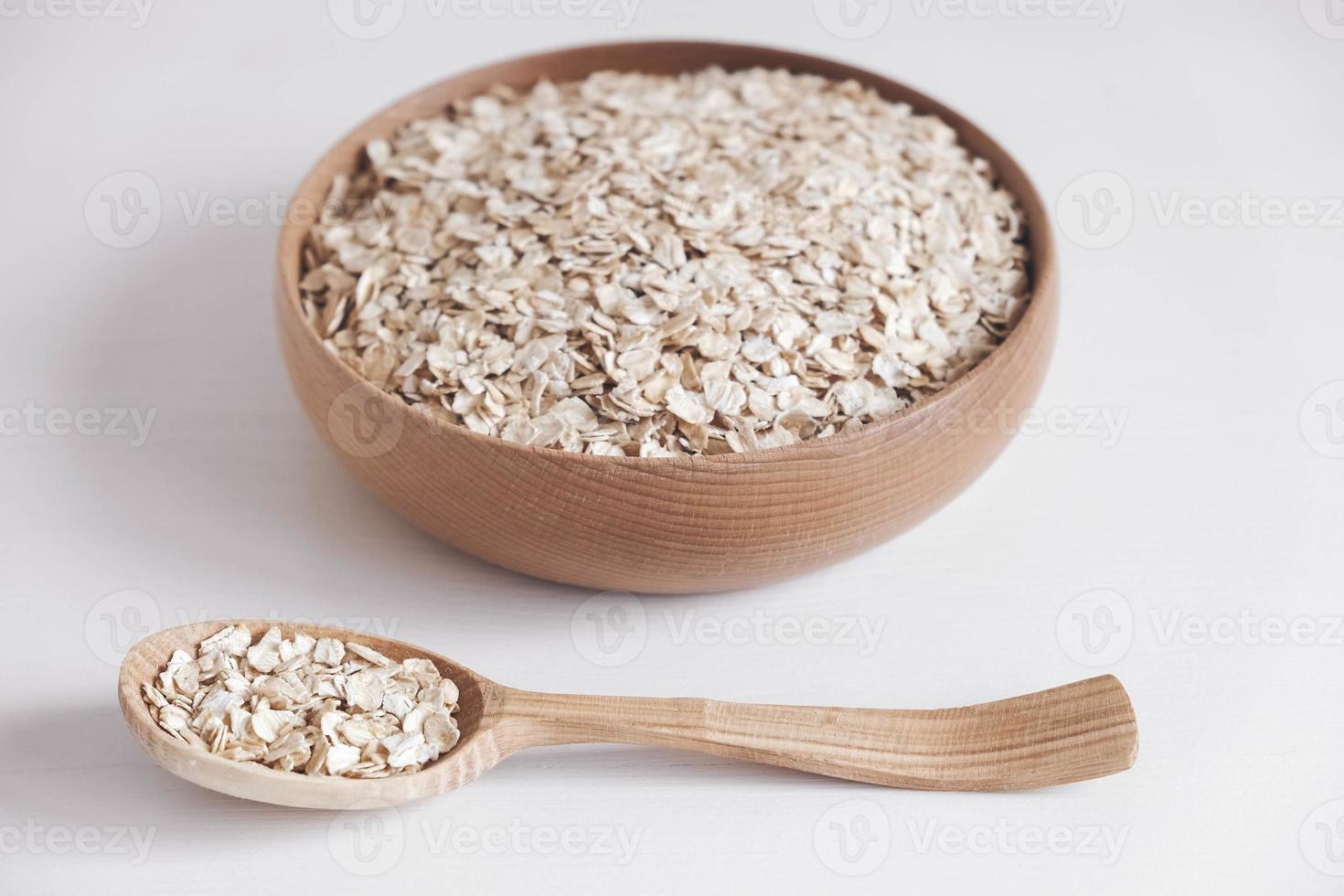 Dry oatmeal in a wooden plate and spoon on a white background photo