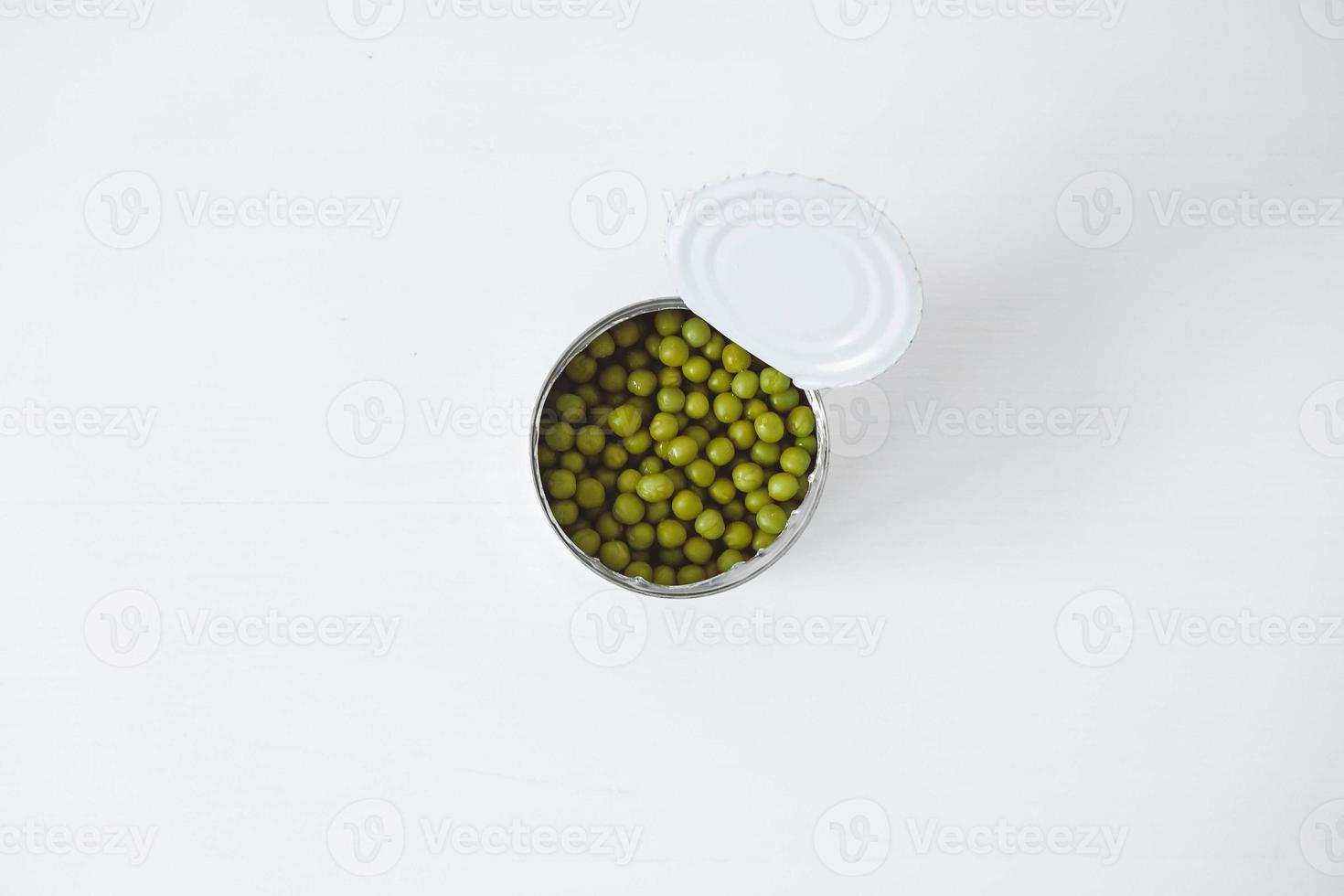 Canned green sweet peas in an open aluminum metal can on a white table. Top view. Copy, empty space for text photo