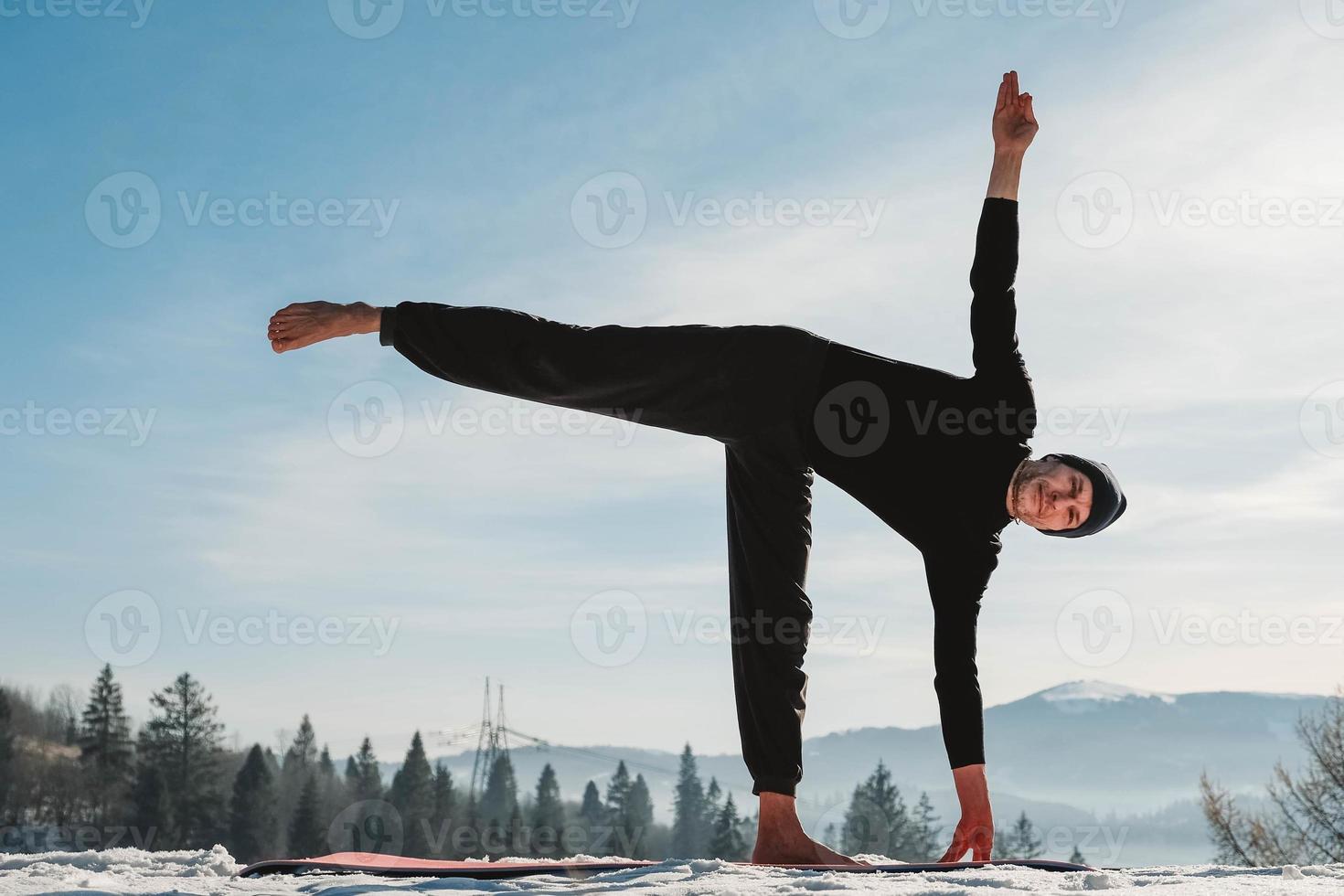 Man practicing yoga and balancing exercises in the winter mountains and enjoying life. Copy, empty space for text photo