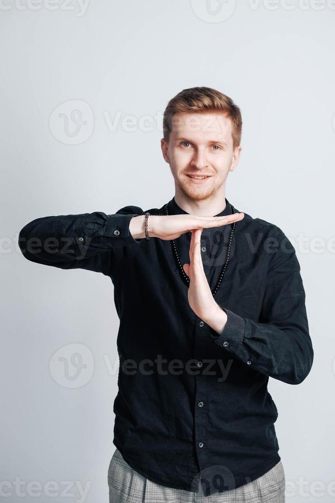Young man in a black shirt shows a time out sign with his hands on a white background. Copy, empty space for text photo