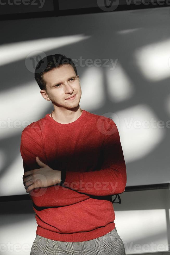 Young man in a red sweater on a white background with shadows from the light. Copy, empty space for text photo