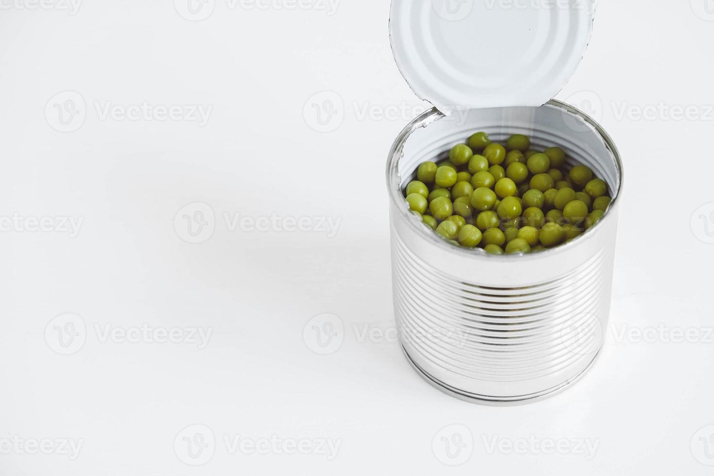 guisantes dulces verdes enlatados en una lata de metal de aluminio abierta sobre una mesa blanca. copiar, espacio vacío para texto foto