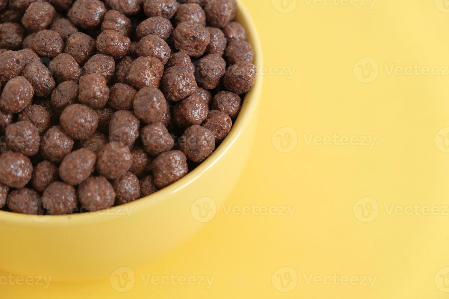 Chocolate cereal corn balls in a yellow bowl on a yellow background. Top view. Copy, empty space for text photo
