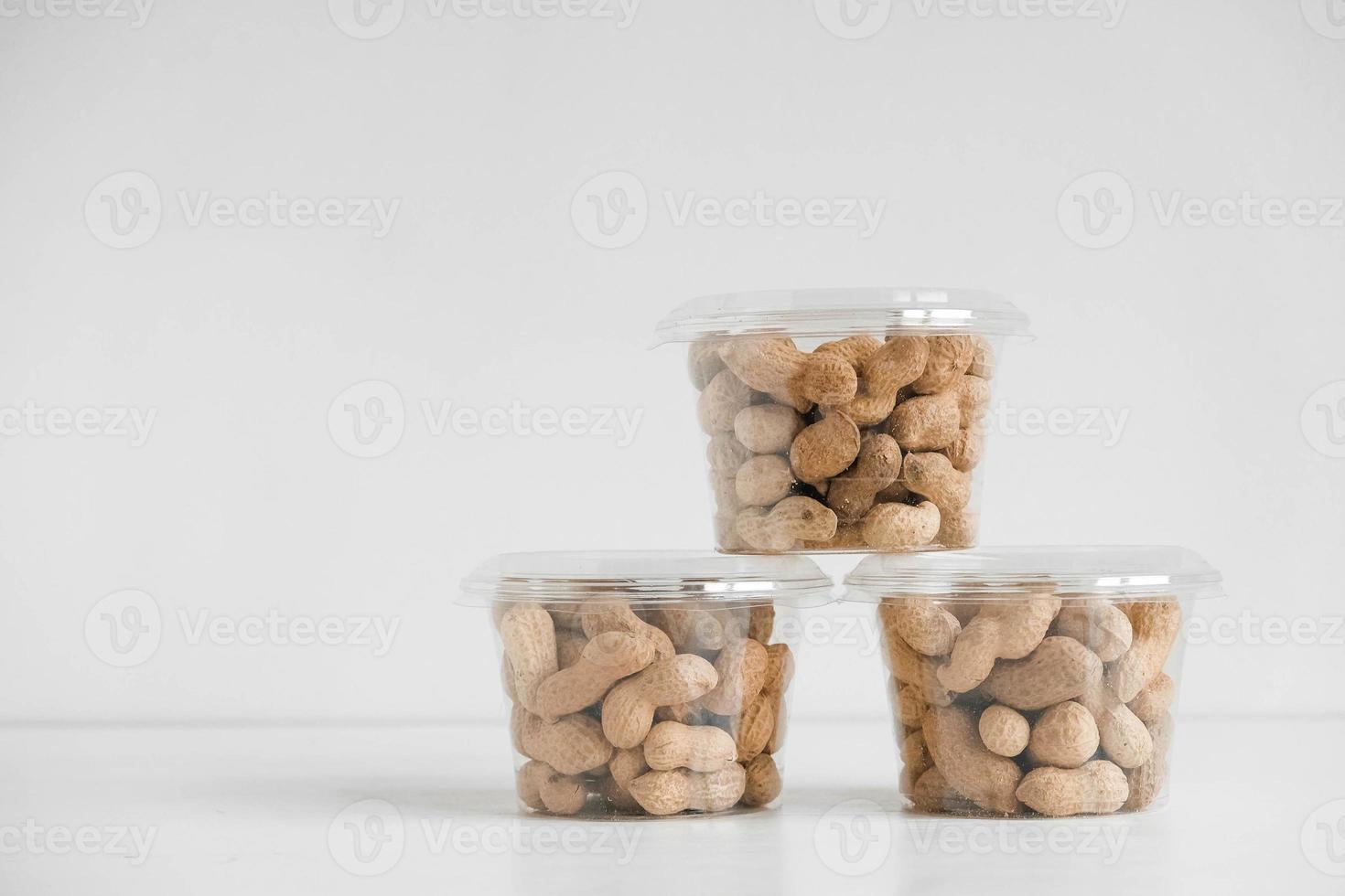 Inshell peanuts in three transparent plastic bowls on a white table photo