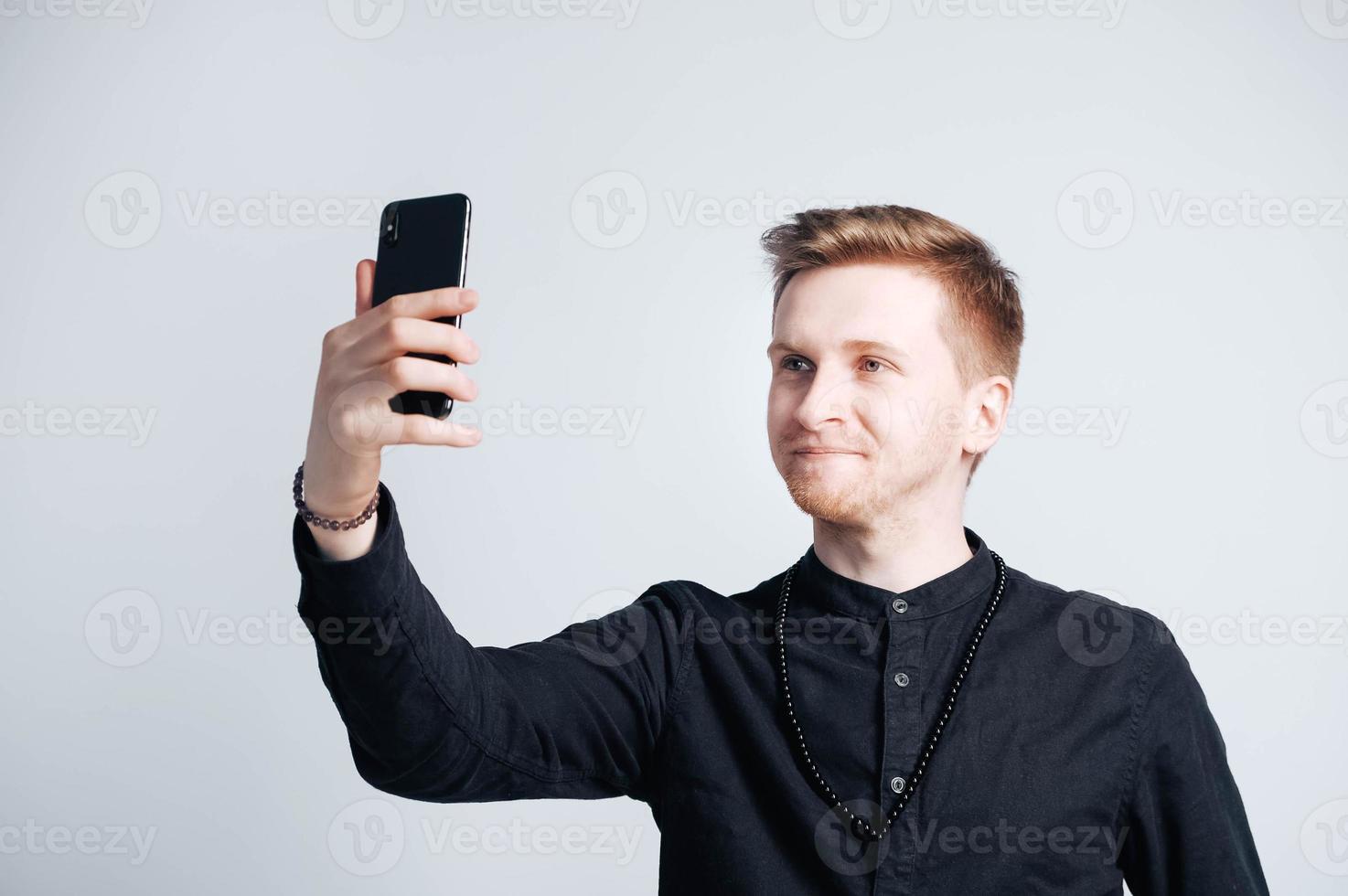 Portrait young man in a black shirt with a smartphone in his hands on a white background photo