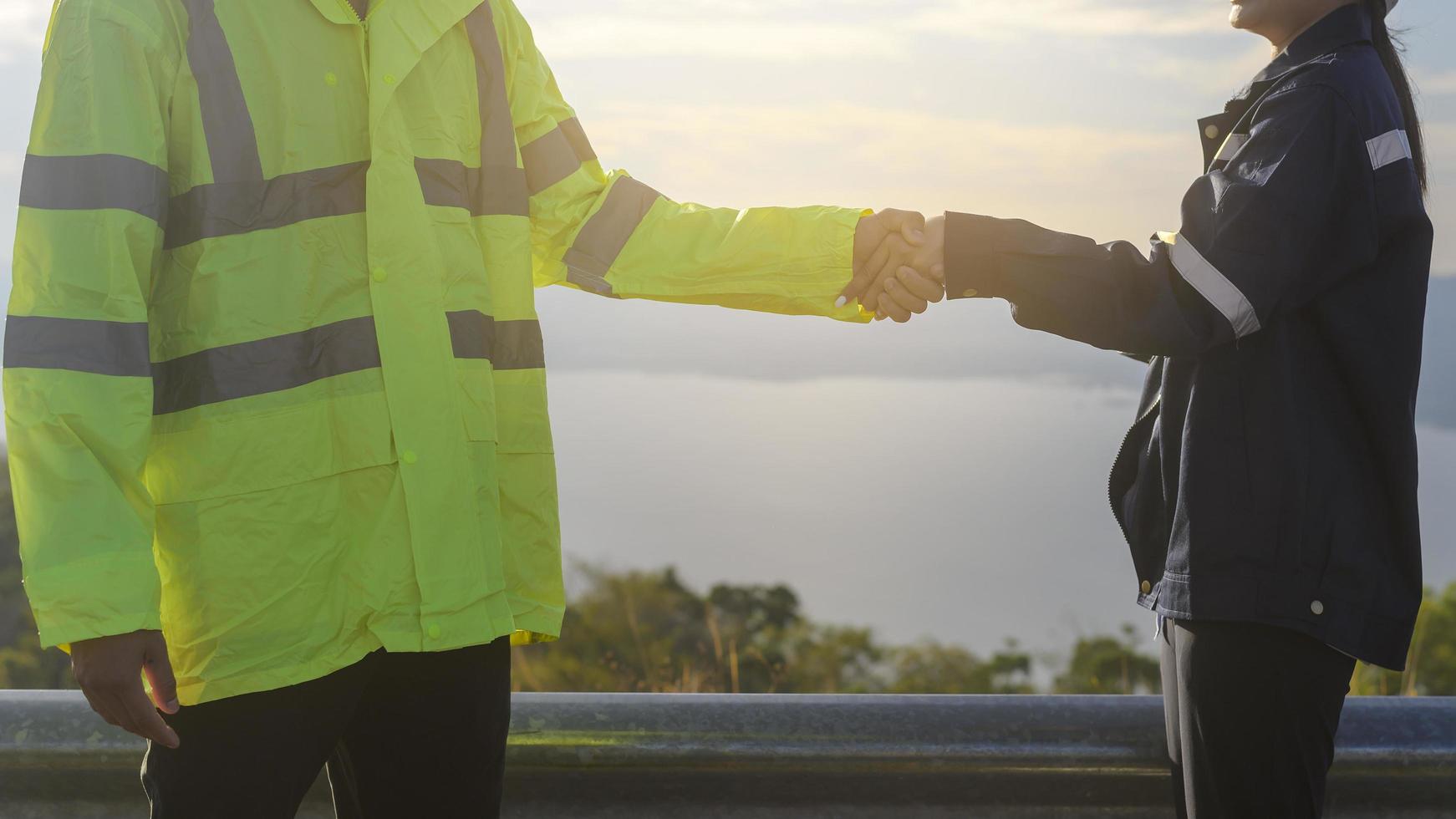 people engineer are shaking hand in a field wearing a protective helmet on her head over electrical turbines background . photo