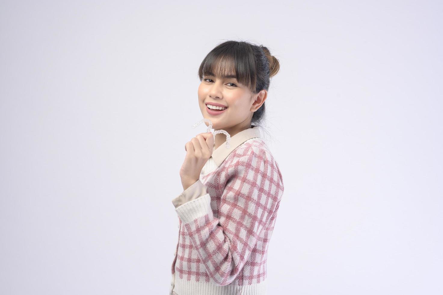 Young smiling woman holding invisalign braces over white background studio, dental healthcare and Orthodontic concept. photo