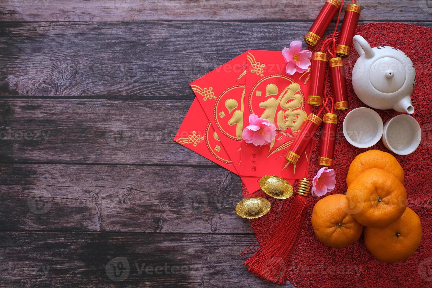 Chinese New Year festival concept. Mandarin oranges, red envelopes, gold ingots and tea pot on red cloth with old wooden background. Chinese character fu which stands for luck photo