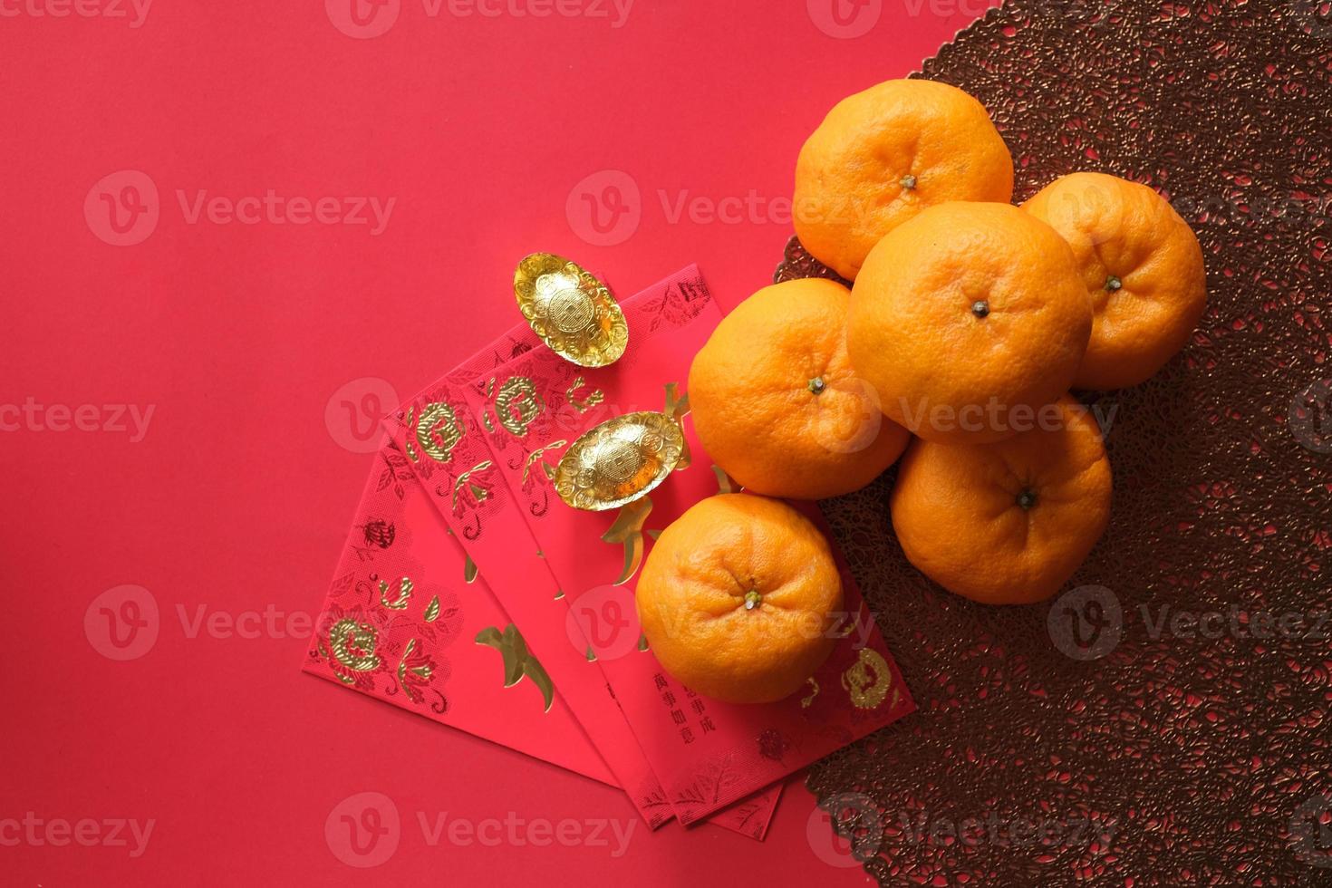 Chinese New Year festival concept. Mandarin oranges, red envelopes, and gold ingots on red cloth with red background. photo