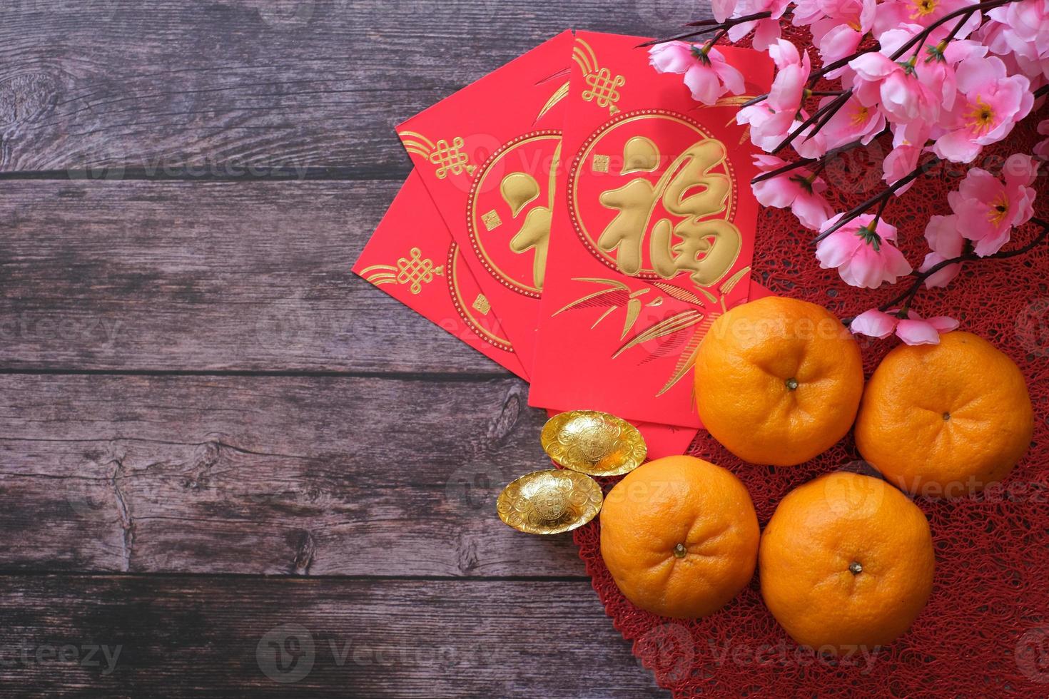 Chinese New Year festival concept. Mandarin oranges, red envelopes, and gold ingots on red cloth with old wooden background decorated with plum blossom. Chinese character fu which stands for luck. photo