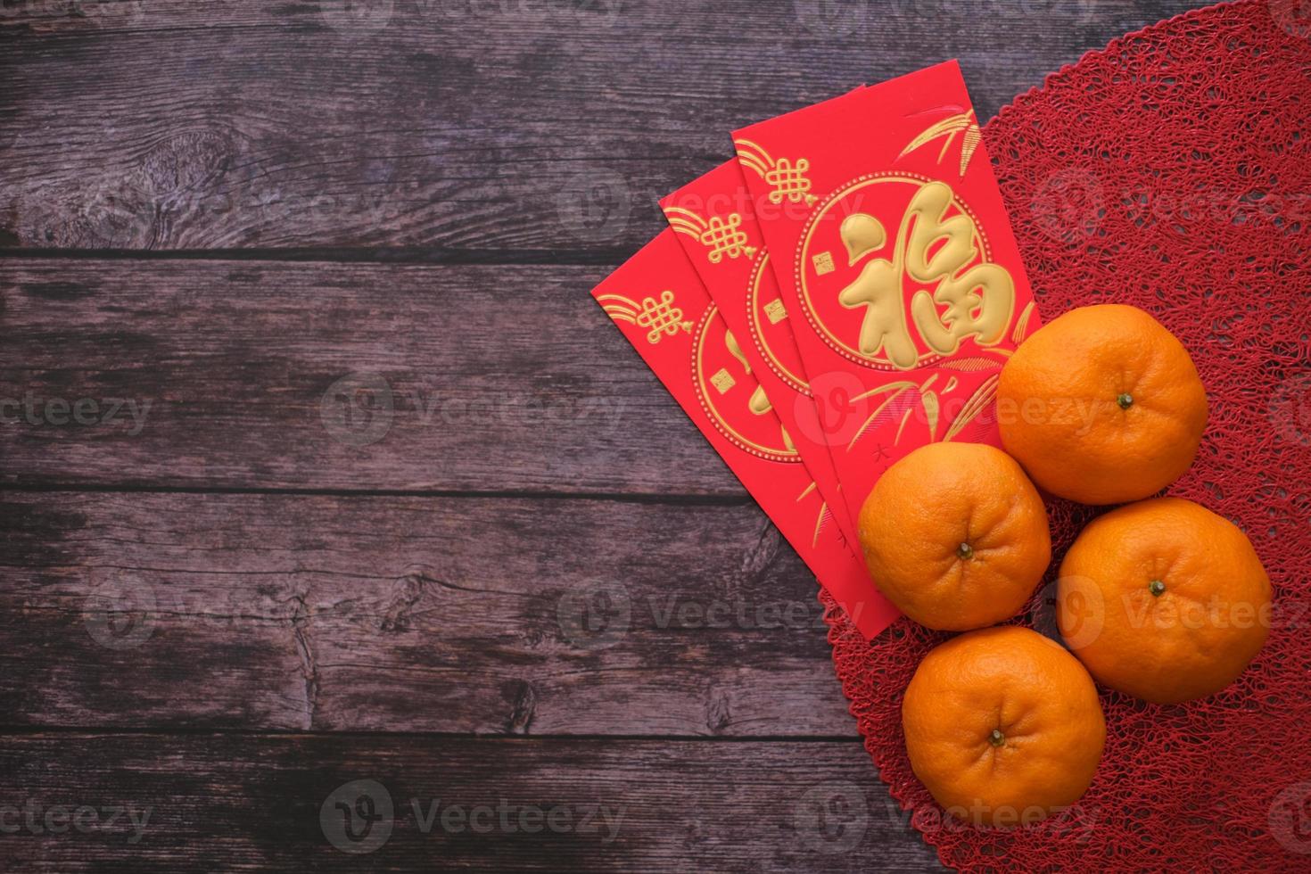 concepto de festival de año nuevo chino. mandarinas y sobres rojos tela roja con fondo de madera vieja. los caracteres chinos significan rico, rico, saludable y feliz. copie el espacio para el texto. foto