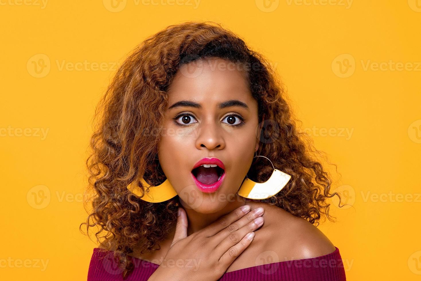 Close up portrait of astonished and surprised young beautiful African American woman looking at camera with mouth open in isolated studio yellow background photo