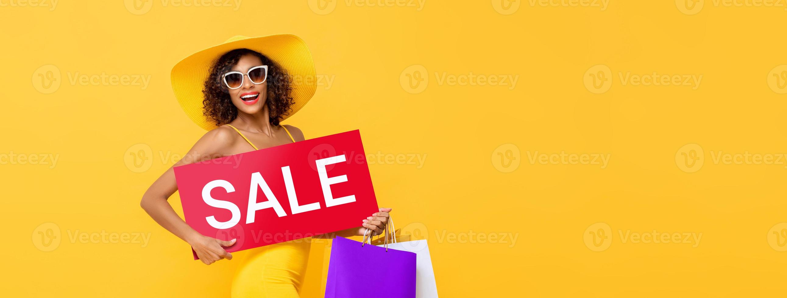 mujer afroamericana con cartel de venta rojo con bolsas de compras aisladas en el fondo de la pancarta amarilla de estudio con espacio de copia foto