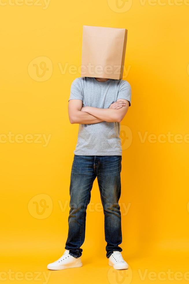 concepto retrato completo de un hombre anónimo con la cabeza cubierta con una bolsa de papel haciendo un gesto de brazos cruzados en el fondo amarillo del estudio foto