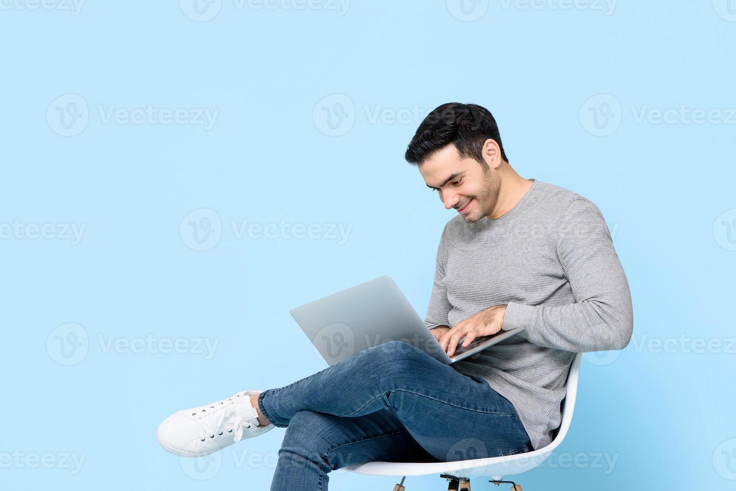 Work from home concept portrait of happy young handsome Caucasian man sitting and using laptop in isolated studio blue background photo