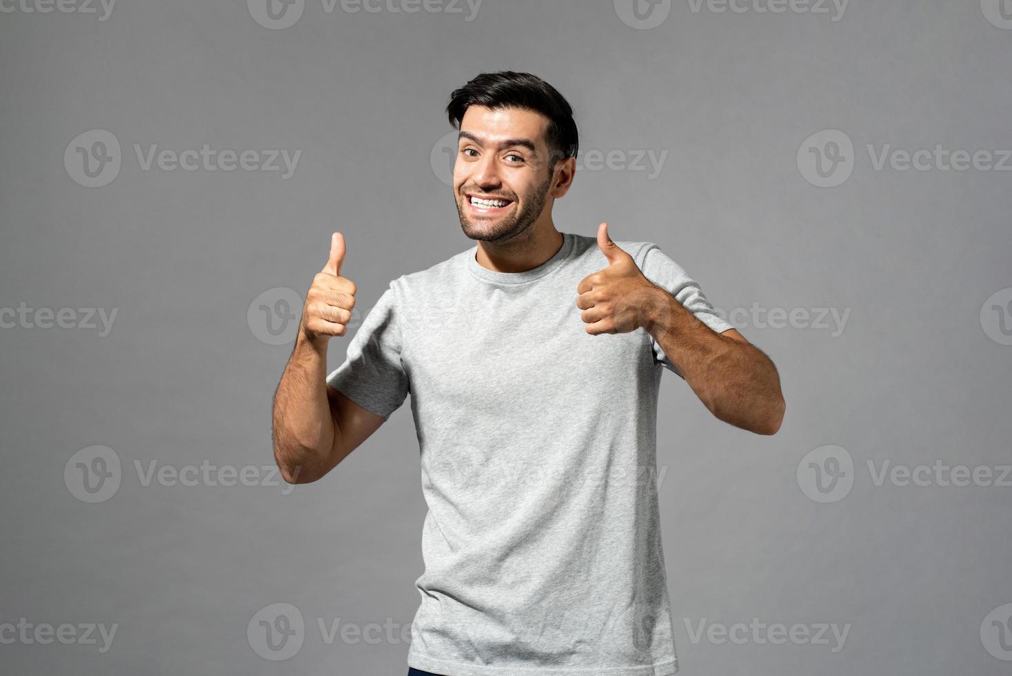 sonriente sorprendido joven caucásico milenario con doble pulgar hacia arriba gesto sobre fondo de estudio gris claro aislado foto