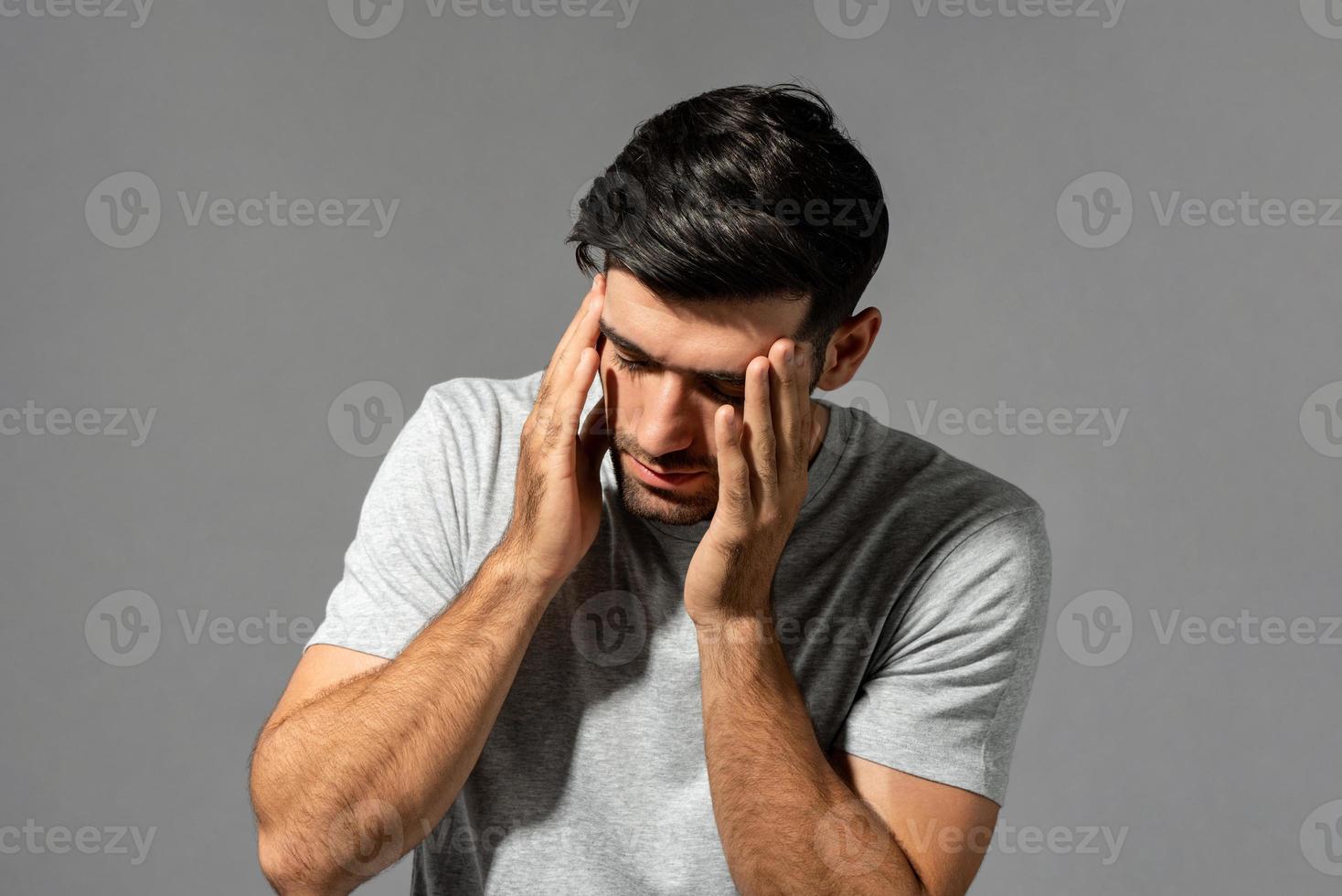 Fatigued young Caucasian man feeling headache, studio shot in isolated gray background photo