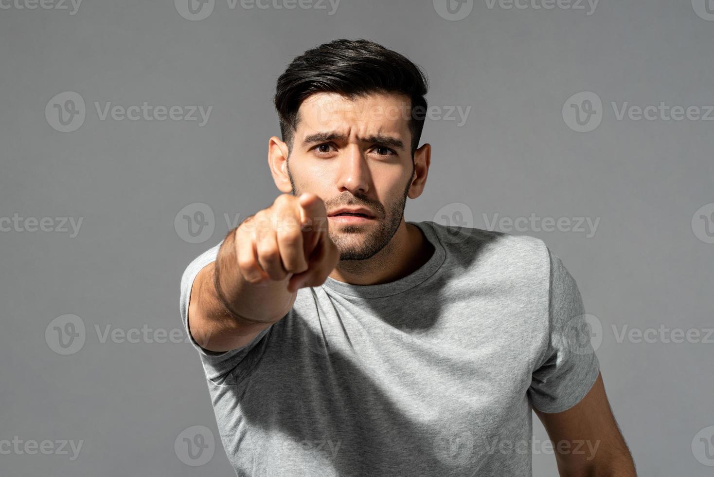 Young handsome Caucasian man looking and pointing finger at you in isolated light gray studio background photo