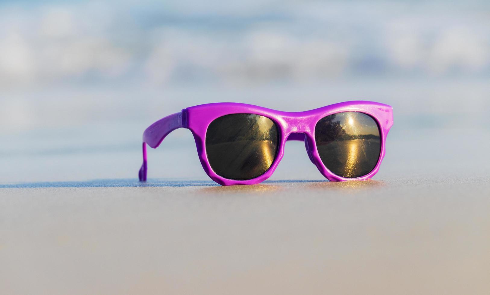 gafas de sol de moda púrpura en la arena hermosa playa de verano foto