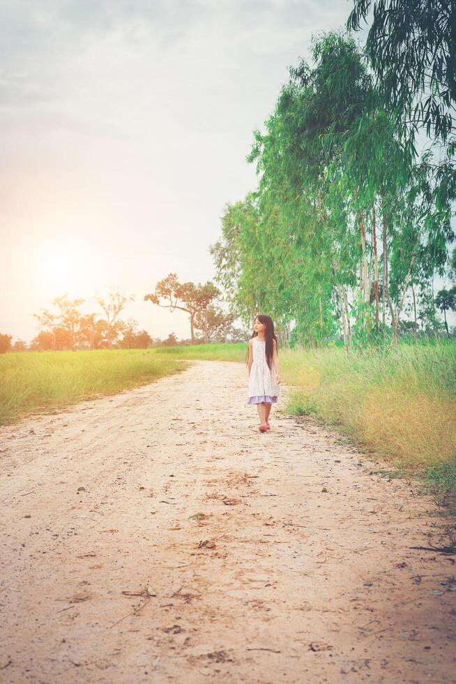 una niña pequeña con el pelo largo vestido se aleja de ti por un camino rural. foto