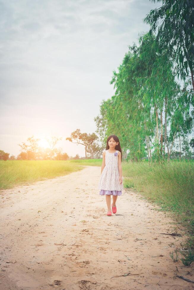 Little girl wearing dress is walking and look away from down rural road. photo