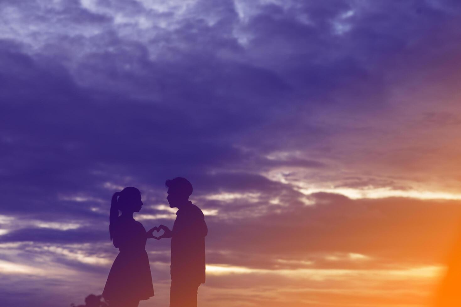 hombre y mujer cogidos de la mano en forma de corazón en el fondo del atardecer. foto