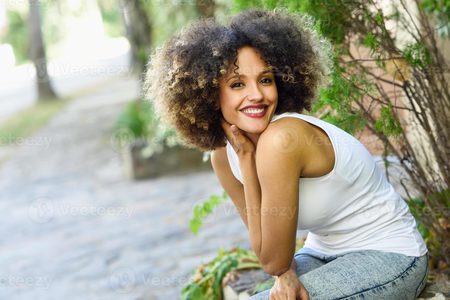 joven negra con peinado afro sonriendo en un parque urbano foto