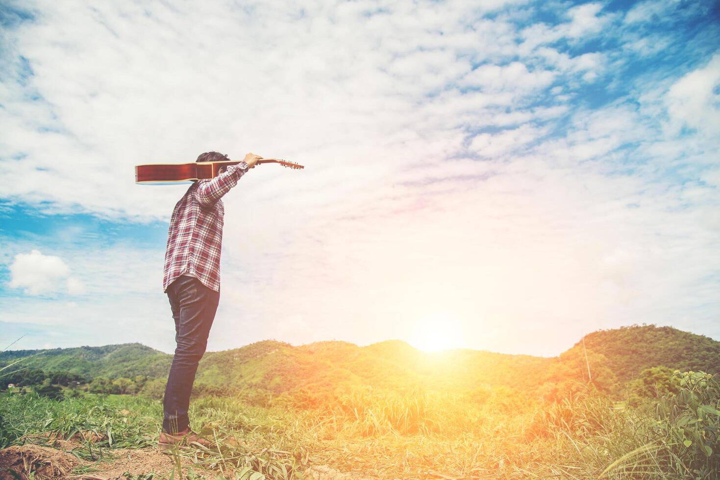 Young hipster man holding a guitar with a walking in nature, Relaxing in the field in a sunny blue sky day. photo