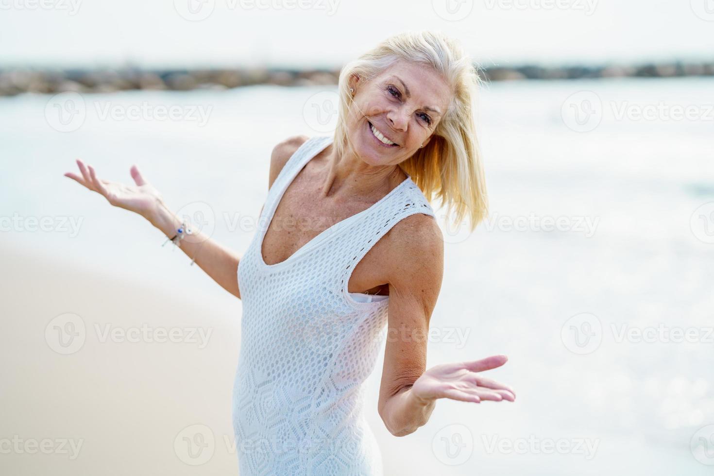 Smiling mature woman walking on the beach, spending her leisure time, enjoying her free time photo