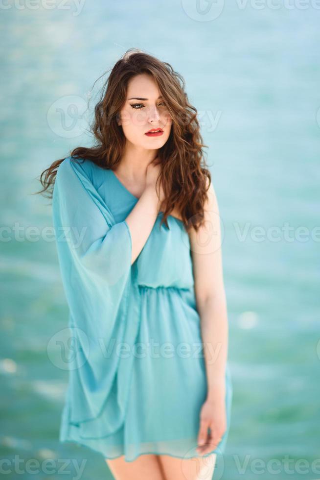 Woman with blue eyes wearing blue dress in the beach. photo