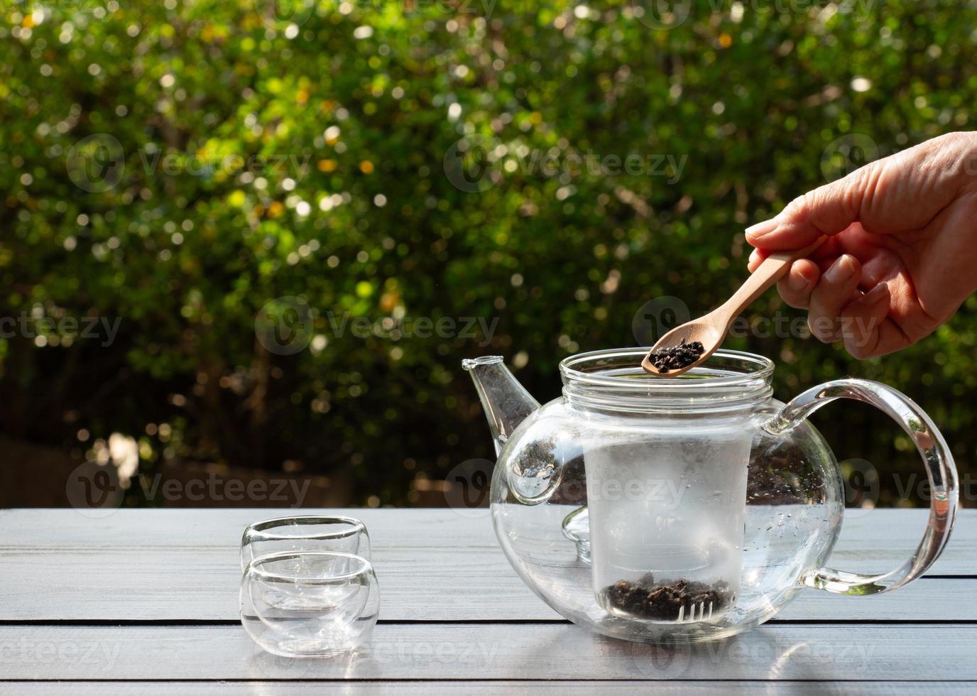 mujer agregando hojas de té a la tetera para hacer té caliente foto