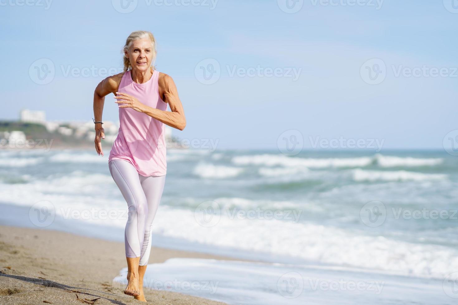 mujer mayor haciendo deporte para mantenerse en forma. mujer madura corriendo por la orilla de la playa. foto
