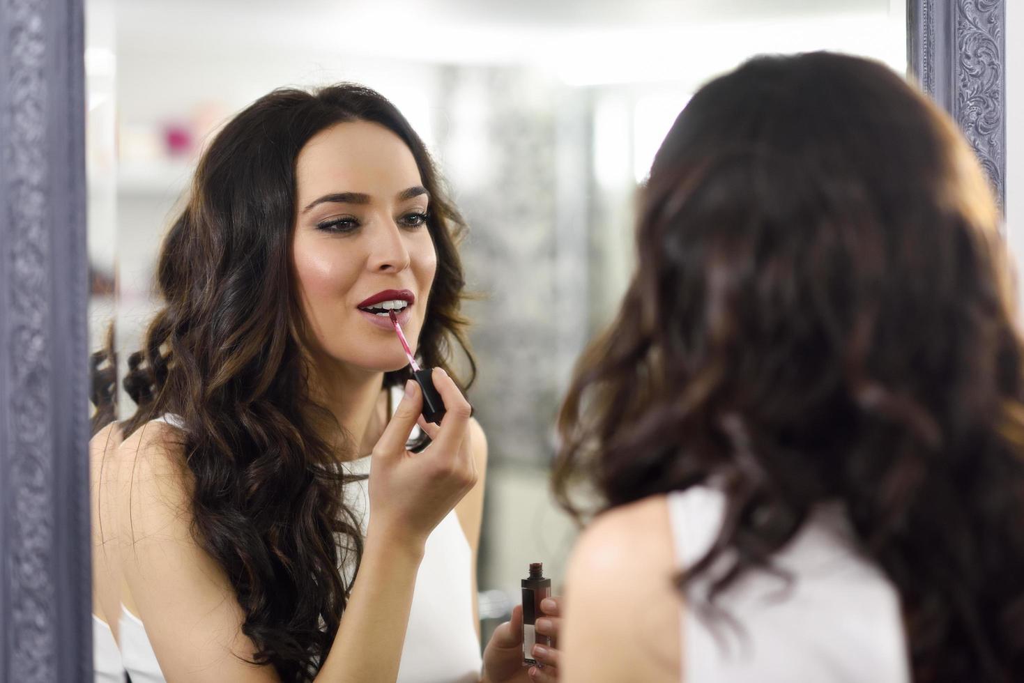 Young woman aplying pink lipstick in front of a mirror photo