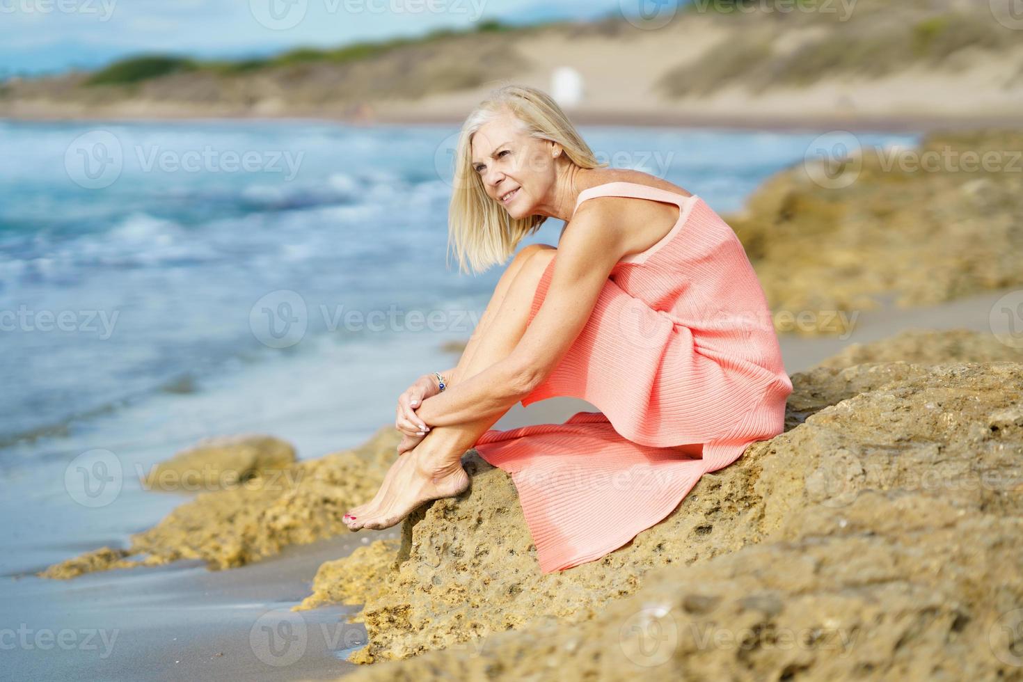 Slim senior woman on rocky seashore in summer photo