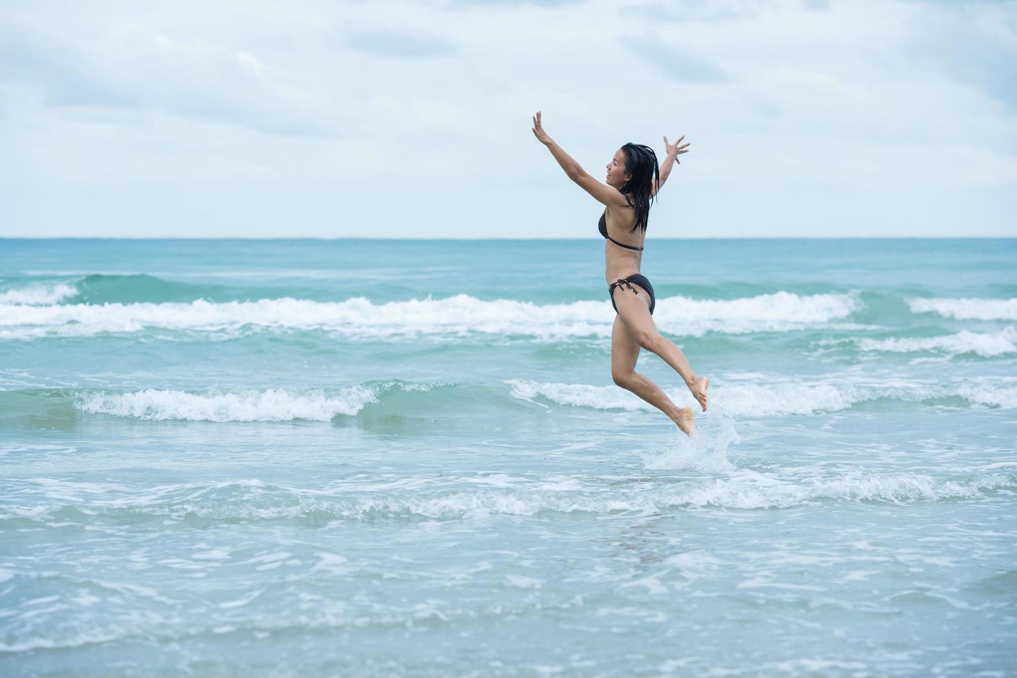 mujeres de belleza con bikini de traje de baño marrón saltando en una playa y mar de olas foto