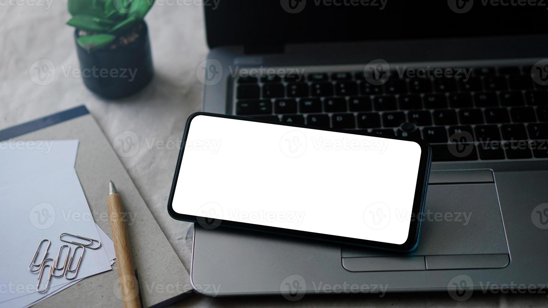 Mobile phone mockup template with white screen on a laptop for remote working and home office concept photo