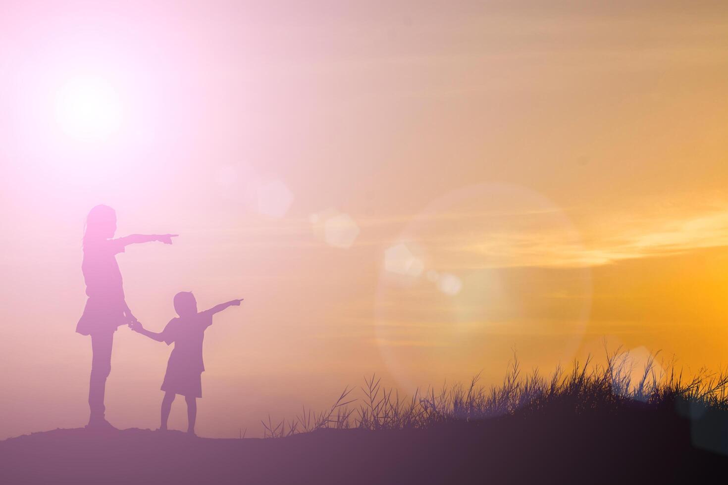 silhouette mother and son at sunset , pointing at the sun photo