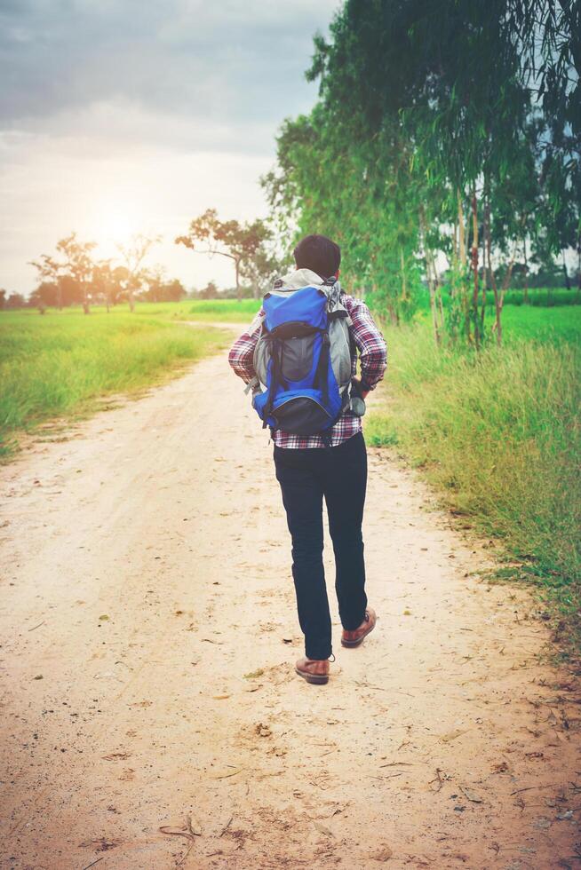 Close up young hipster man with backpack on his shoulder walking down countryside. photo