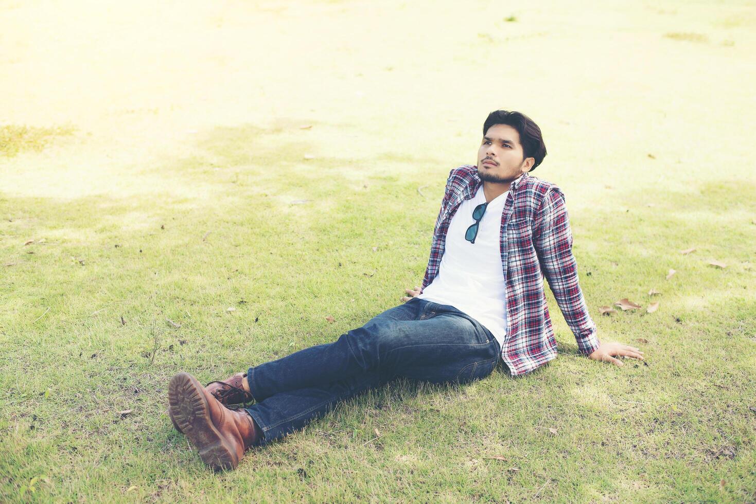 Young hipster man sitting on the grass in the park, Enjoy with natural and fresh breeze air. photo