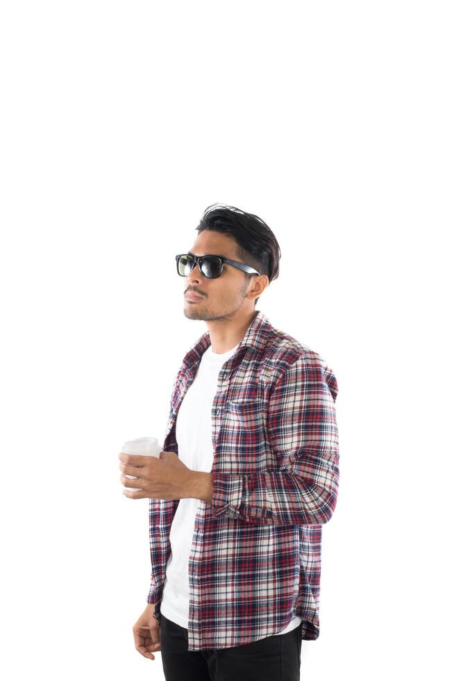 Portrait of handsome young hipster man standing ,wearing sunglasses, shirt and holding cup of coffee on isolated white background. photo