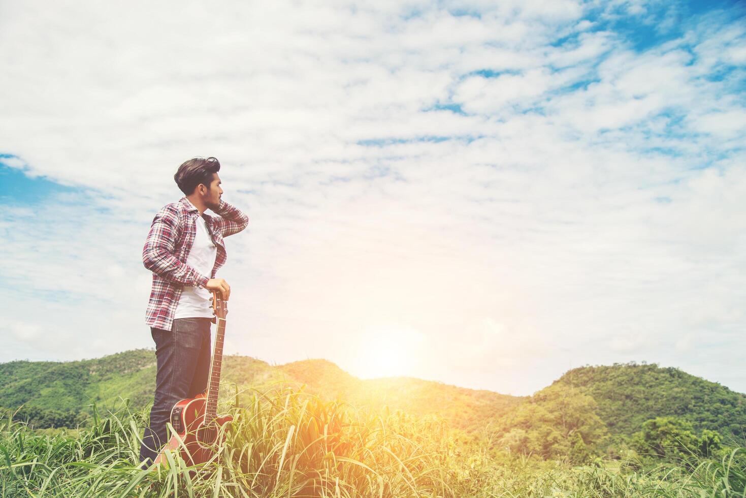 Young hipster man holding a guitar with a walking in nature, Relaxing in the field in a sunny blue sky day. photo