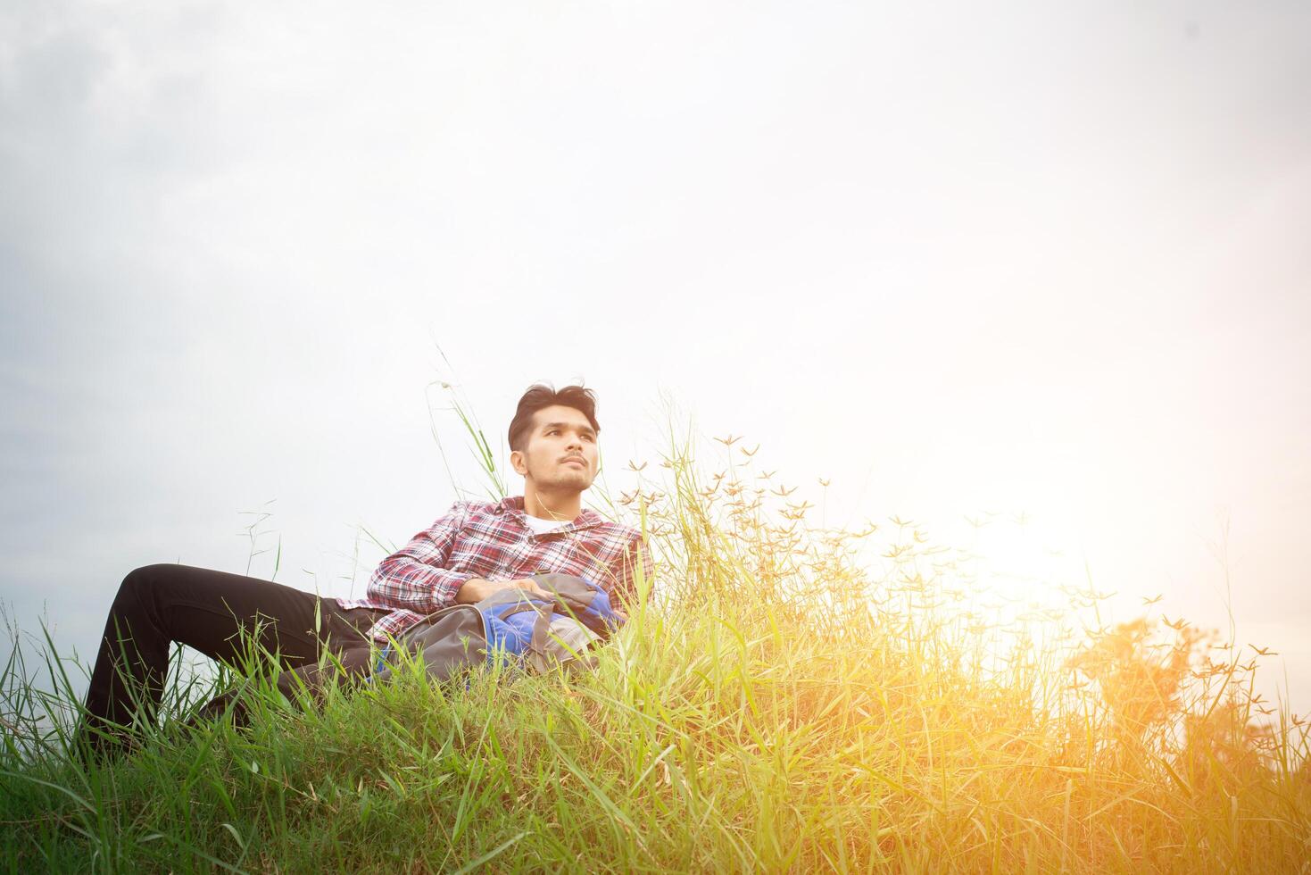 el joven hipster descansa en los prados después de caminar, mira hacia otro lado para encontrar otra aventura. foto