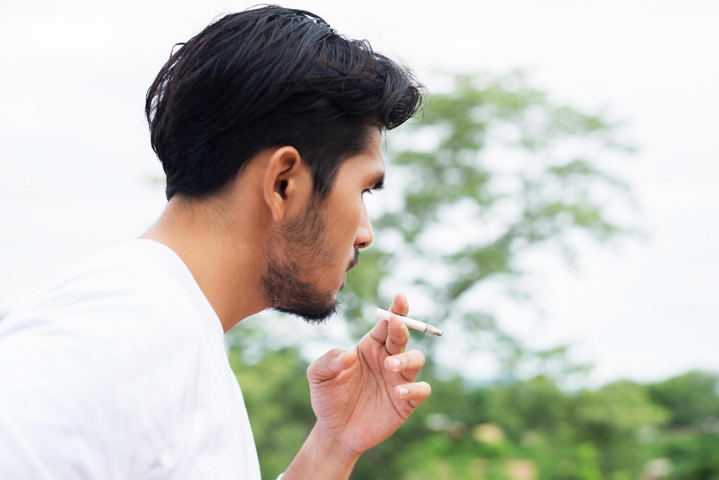 Young hipster man taking rest, smoking cigarette with nature and fresh breeze. photo