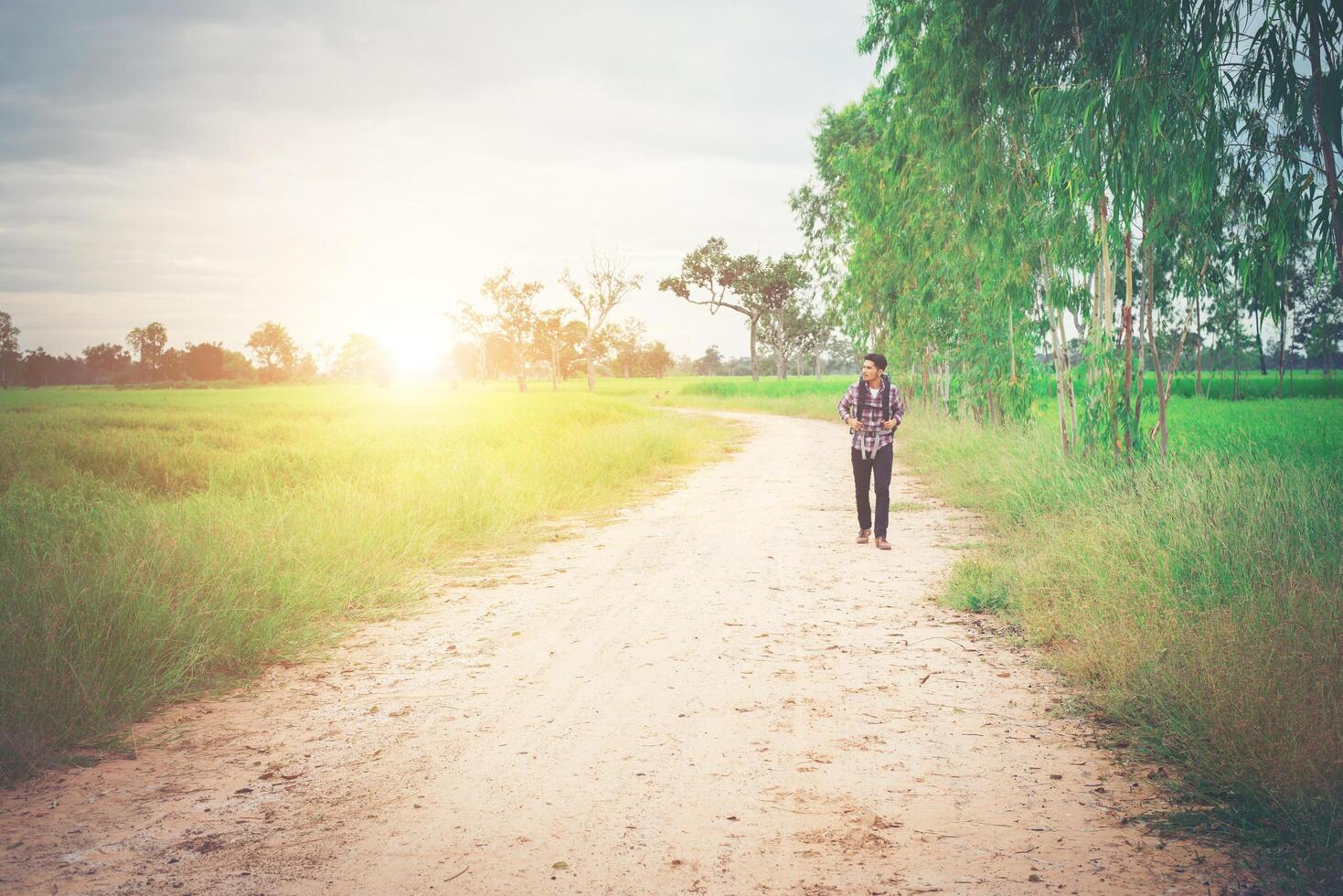 espalda de un joven hipster con mochila en el hombro caminando por el campo. foto