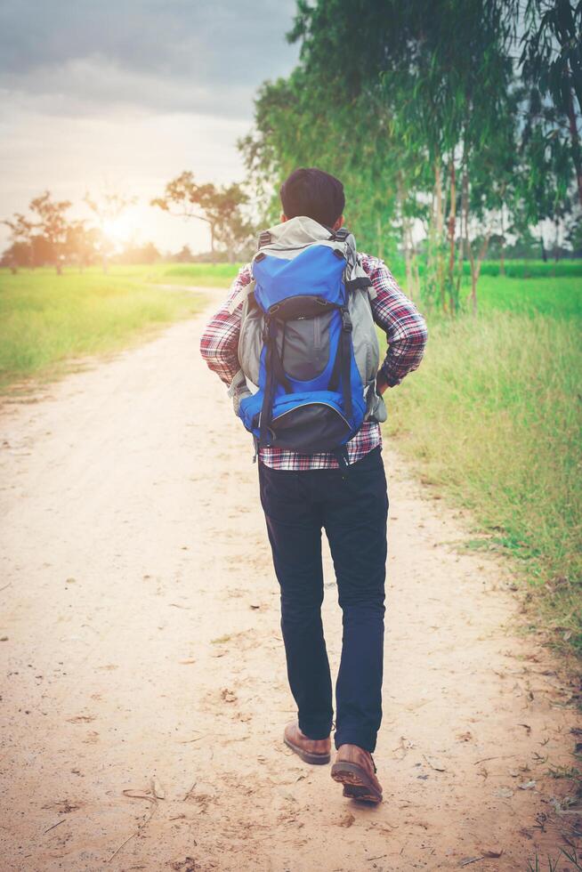 Close up young hipster man with backpack on his shoulder walking down countryside. photo